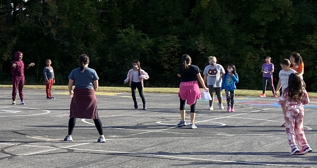two coaches and several girls play on the blacktop