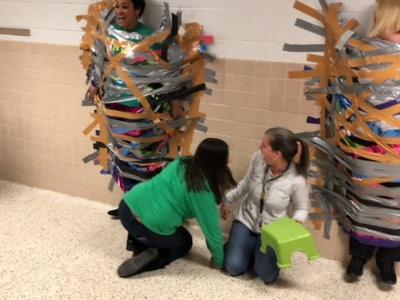 photo of teacher removing stool from under people taped to the wall